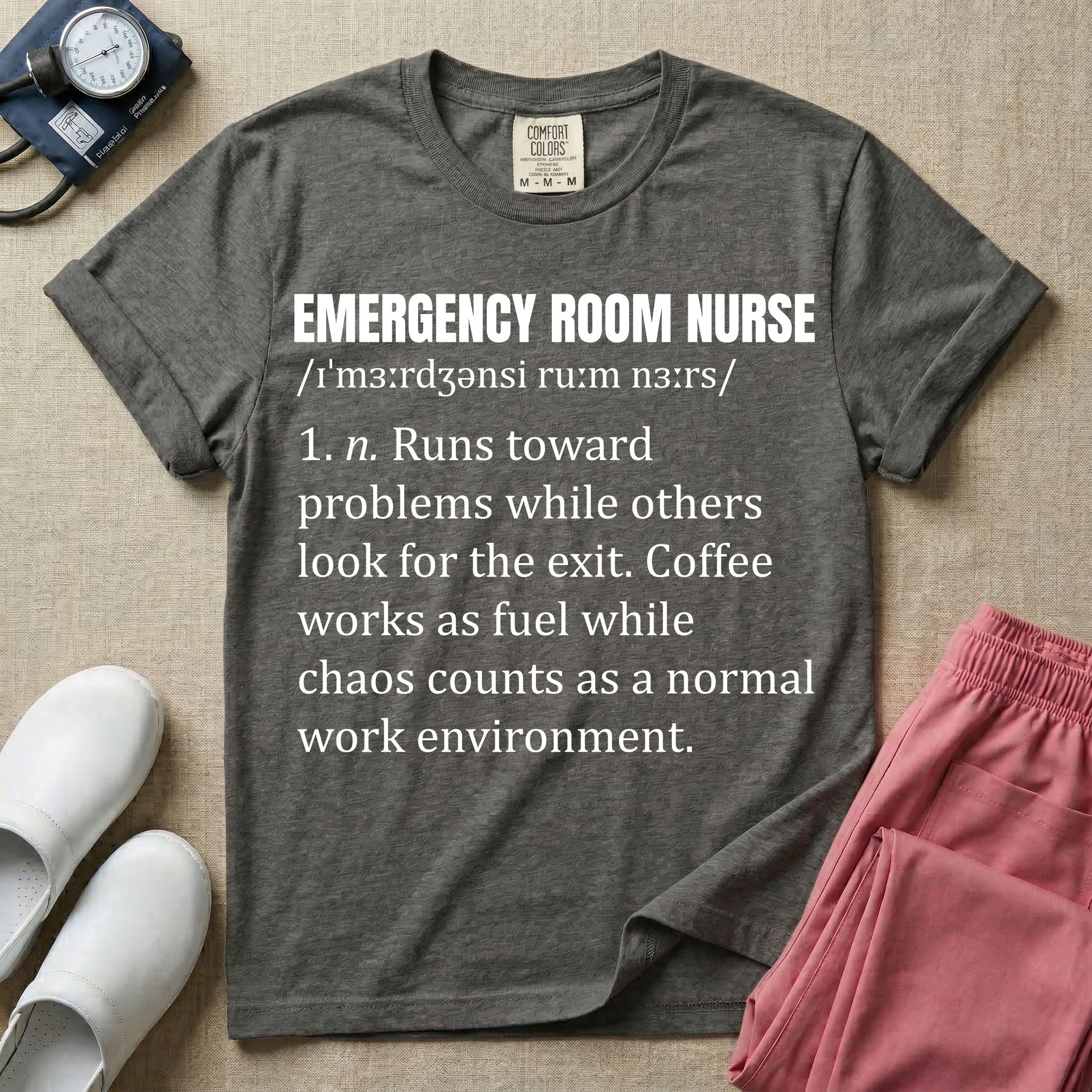 A minimalist t-shirt for emergency room nurses featuring a dictionary definition graphic for the term "EMERGENCY ROOM NURSE" with a phonetic pronunciation and a humorous description about running toward problems, using coffee as fuel, and thriving in chaos.