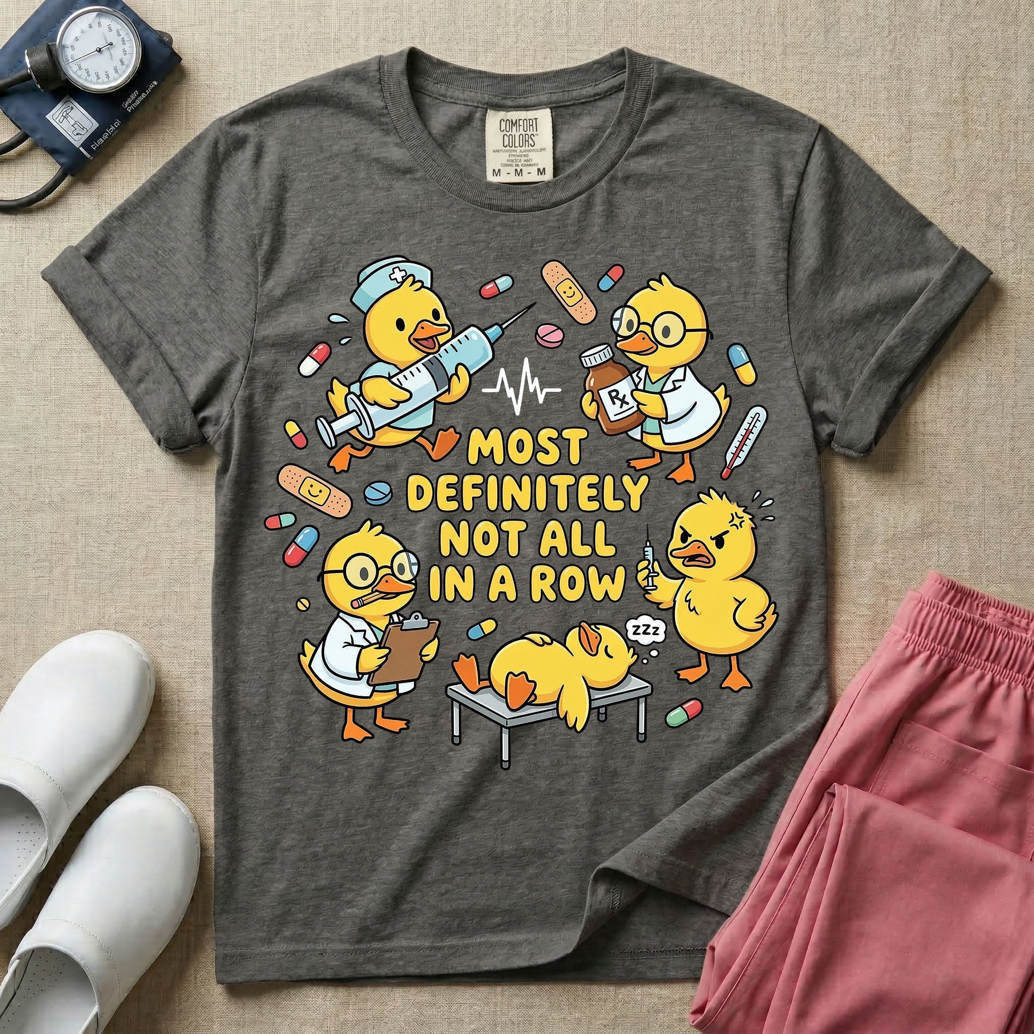 General nursing t-shirt featuring a chaotic group of cartoon ducklings dressed as medical professionals with the text "MOST DEFINITELY NOT ALL IN A ROW" on a sage green garment, in pepper color.