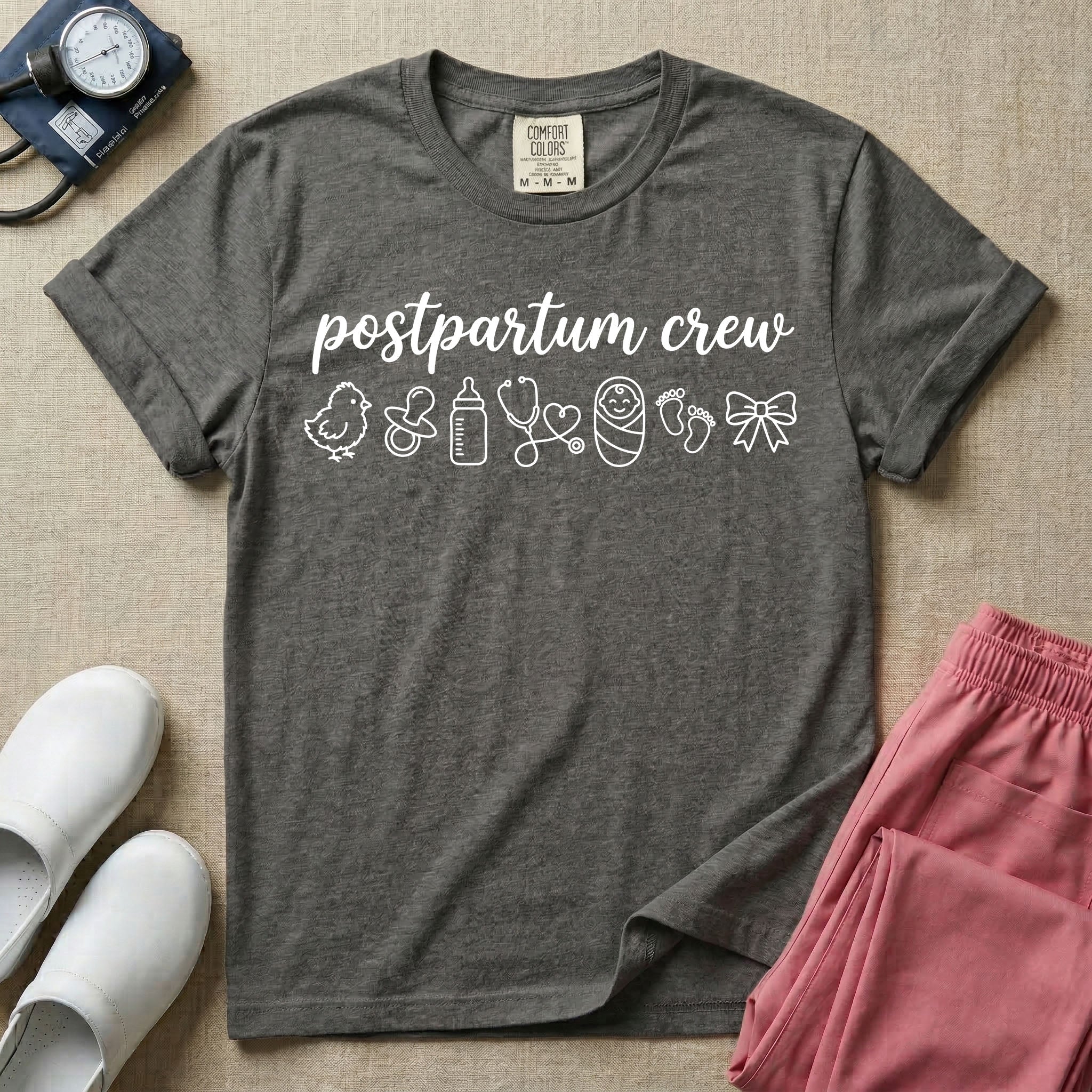 A t-shirt featuring the lowercase text postpartum crew in a cursive script font above a horizontal row of minimalist line-art icons including a baby chick, a pacifier, a baby bottle, a heart-shaped stethoscope, a swaddled baby, baby footprints, and a ribbon bow.