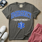 A classic varsity-style t-shirt for emergency room nurses featuring the word "EMERGENCY" in a large, arched blue collegiate font above the word "DEPARTMENT", centered over a blue Star of Life medical symbol.